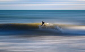 Surfista em pé na prancha pegando uma onda, com o mar ao fundo